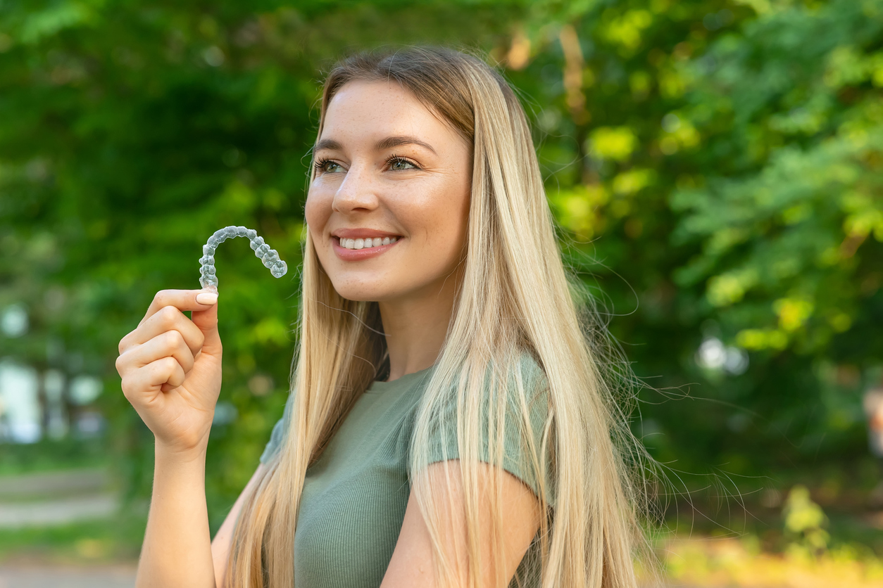 Smiling woman holding up a clear aligner dental tray to highlight the benefits of Invisalign